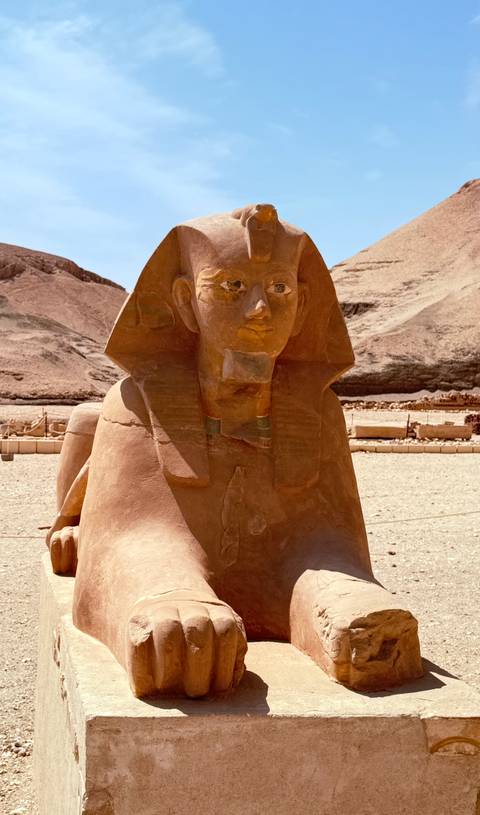 Sphinx-style statue carved from stone displayed in an open archaeological site.