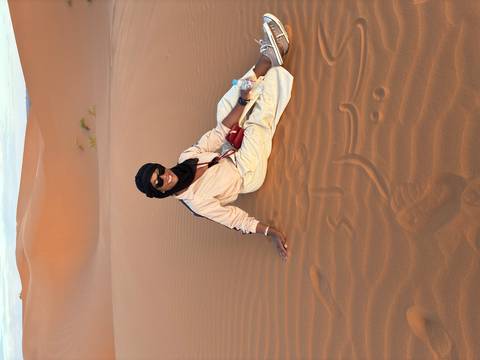 Traveller sitting relaxed on the warm sand of a vast dune holding a water bottle.