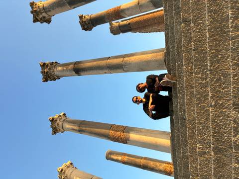 Two travellers sitting on stone steps beneath towering ancient Roman columns at Volubilis.