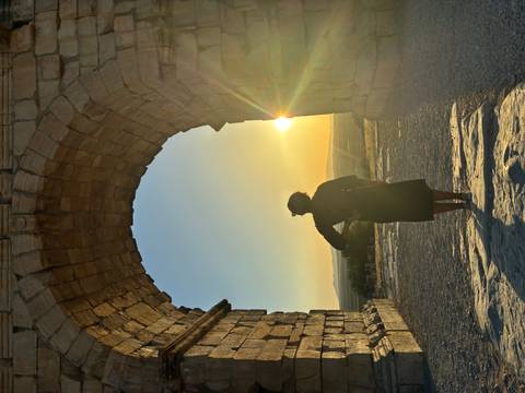 Back-lit view of a woman framed by a stone arch at sunset in Volubilis.