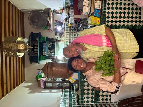 Traveller and local chef smiling in a traditional Moroccan kitchen holding fresh herbs.