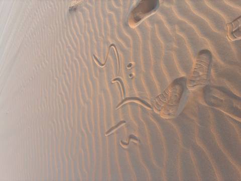 Arabic words and footprints etched into rippled desert sand.