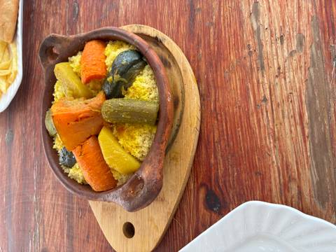 Traditional vegetable couscous tagine in a clay pot on a rustic wooden table.
