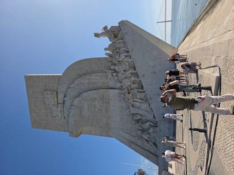 Side view of the Monument to the Discoveries with tourists photographing the stone carvings under bright sun