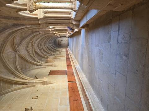 Long vaulted stone cloister corridor with ribbed ceilings and soft directional light creating deep shadows
