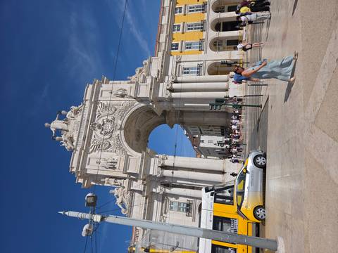 Triumphal Rua Augusta Arch in Lisbon with yellow tram and crowds beneath a clear blue sky