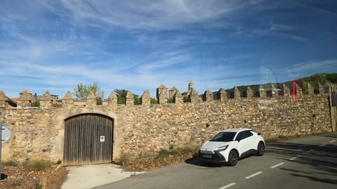 Stone defensive wall with crenellations beside a narrow road where a white car is parked under blue sky