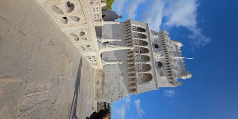 Upward perspective of Belém Tower’s limestone façade and battlements against vivid blue sky