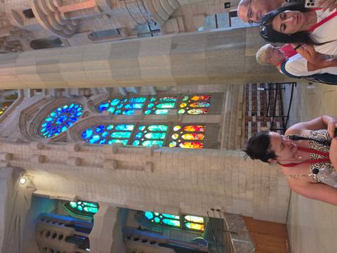 Interior of Sagrada Família with vivid multicolored stained glass windows and visitors listening to a guide