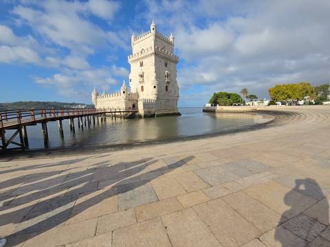 Belém Tower seen across calm water with curved stone promenade and long shadows of visitors