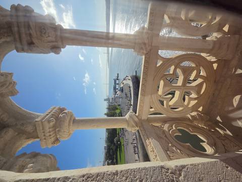 Ornate stone balcony of Belém Tower framing a bright river view and distant bridge under morning sun