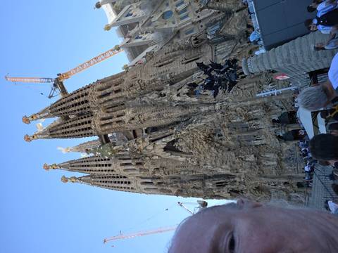 Exterior façade of La Sagrada Família with construction cranes and queueing visitors viewed from street level