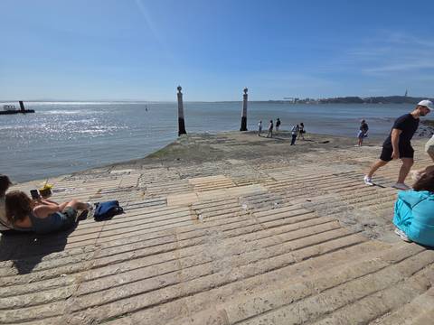 Stone steps leading into the Tagus River where locals relax in the sun, swimmers and walkers nearby