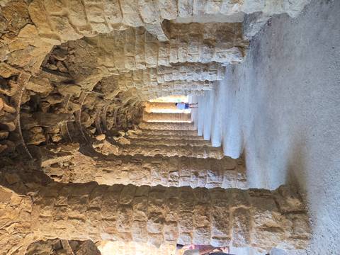 Stone colonnade tunnel with repeating arches in Park Güell, one visitor walking into the distance
