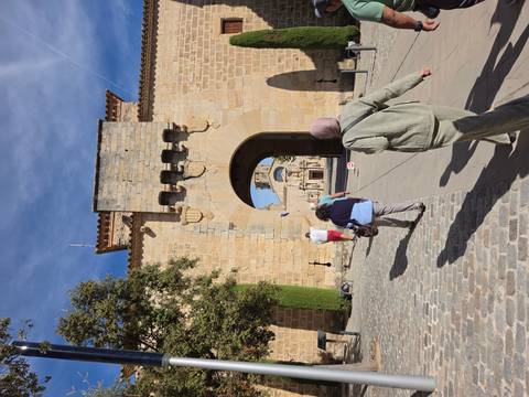 Visitors walking through a stone gateway into a historic complex with church visible beyond