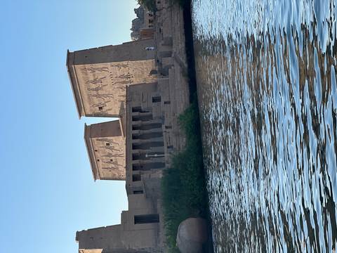 Ancient Philae temple towers with hieroglyphs viewed from water, reflected in Nile