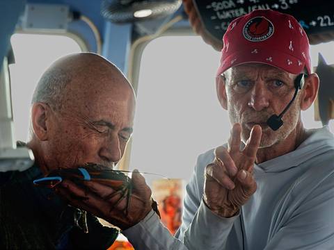 Man playfully kissing a live lobster while a guide explains with headset microphone.