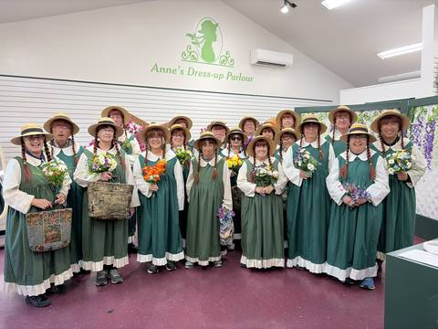 Large group dressed in matching green prairie dresses and straw hats holding bouquets.