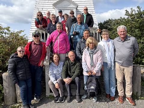 Tour group posing on wooden steps beside a small white lighthouse structure.