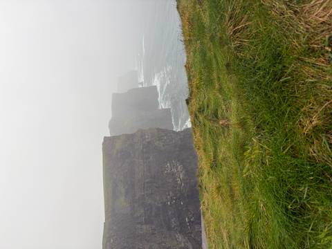Iconic sea cliffs disappearing into misty fog with waves crashing below