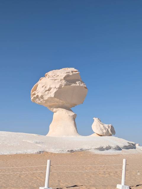 Iconic chalk formation resembling a mushroom stands against clear blue sky in Egypt’s White Desert.