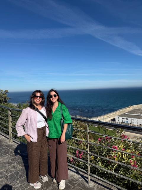 Two women pose at a coastal viewpoint with blue Atlantic waters stretching to the horizon.