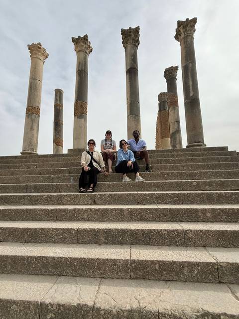 Four travellers sit on ancient stone steps between Roman columns posing for the camera.