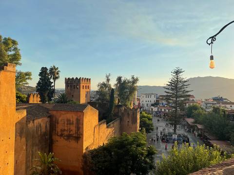 Golden evening light over Chefchaouen’s kasbah and distant mountains with town square below.
