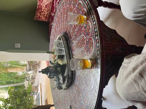 Silver teapot, glasses of amber tea and sweets on an ornate Moroccan table inside a shaded courtyard.