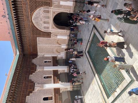 Historic Islamic college courtyard with tile work, arches and a central reflecting pool filled with visitors.