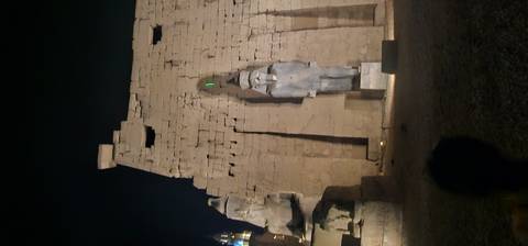 Out-of-focus night view of large stone statues and pylon walls at ancient temple site.