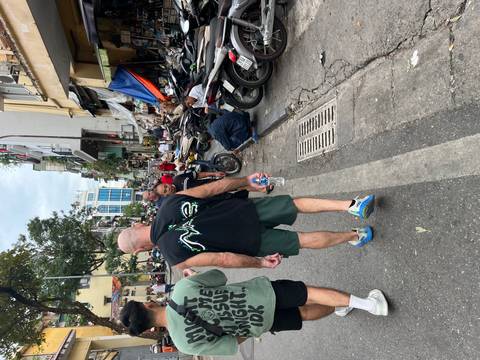 Busy Vietnamese street with motorbikes, vendors and tourists walking past small shops.