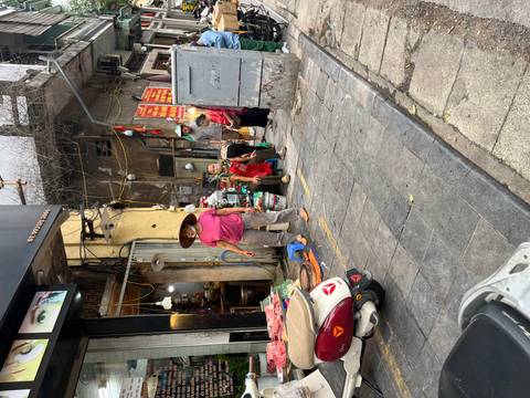 Local market vendors in conical hats sell produce along a narrow pavement.
