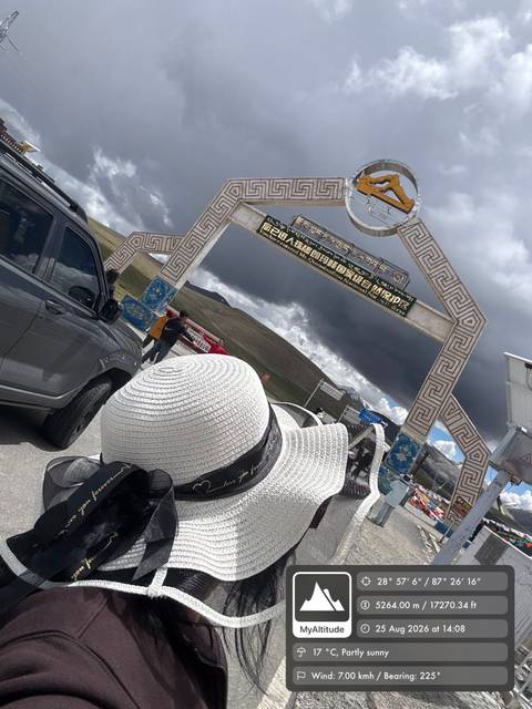 Decorative gate on a high-altitude Tibetan pass with travelers and vehicles nearby under dark clouds.