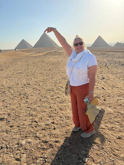Woman stands in desert landscape playfully posing with woven bag and scarf.