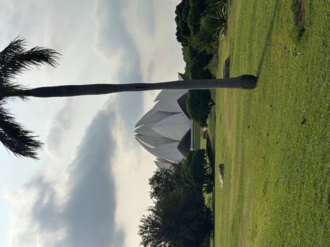 Lotus-shaped white marble temple seen across a green lawn with a palm tree in the foreground