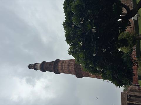 Tall brick minaret rising against a cloudy sky with flowering tree below