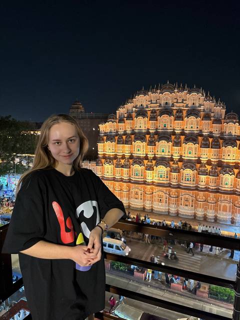 Smiling woman on a balcony overlooking the illuminated Hawa Mahal at night
