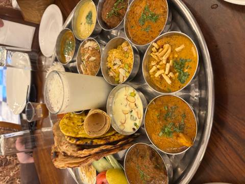 Traditional Indian thali platter with assorted curries, naan, dessert and lassi