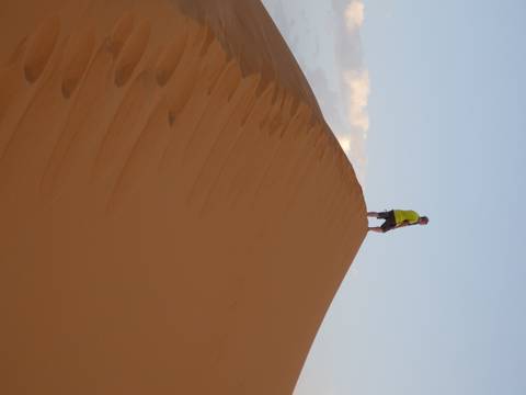 Man standing atop a high orange sand dune at sunset in the Sahara