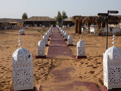 Walkway lined with white lanterns leading to a desert camp tents complex