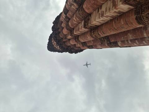 Airplane flying above the historic Qutub Minar against a dramatic cloudy sky