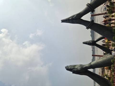 Massive bronze praying-hand statues beside a river under a hazy sky