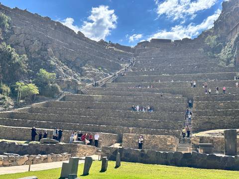 Tourists scale the tiered Inca terraces of Ollantaytambo under bright blue skies.