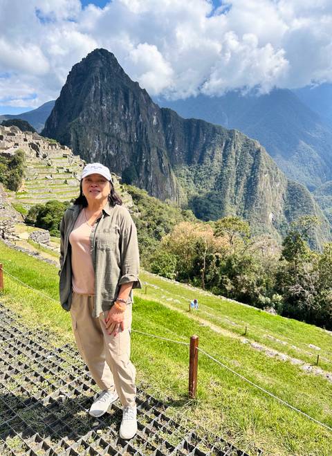 Traveler poses on Machu Picchu terraces with steep green mountains behind.