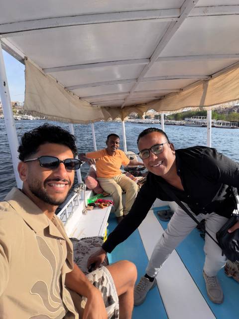 Three men relax on a small open launch cruising the Nile with rocky Aswan hills behind.