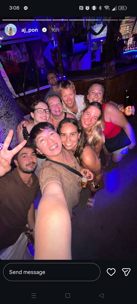 Energetic group selfie at a dimly lit party, travellers smiling and flashing peace signs.