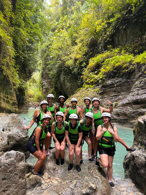 Helmeted adventure group posing in a turquoise canyon river surrounded by lush cliffs.