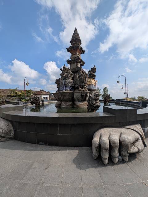 Ornate Balinese fountain with guardian statues surrounded by a reflecting pool under blue skies.