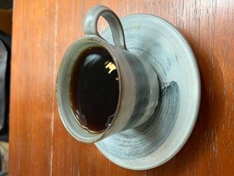 Close-up of a ceramic cup filled with black coffee on a matching saucer placed on a wooden table surface.